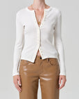 Person wearing a white cardigan and brown pants on a gray background