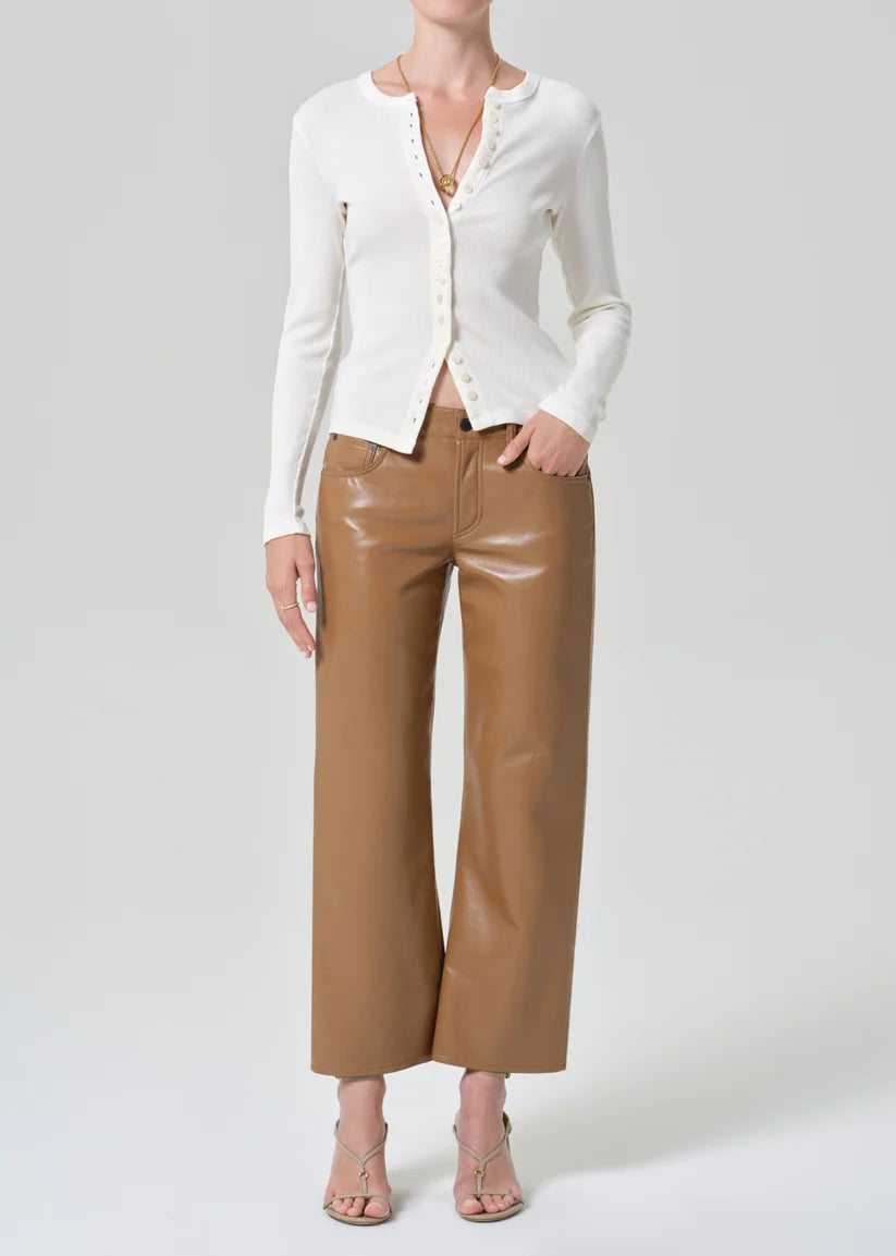 A model wearing a white long-sleeve button-front cardigan, brown wide-leg cropped pants, and beige strappy heels, photographed against a light gray studio background.