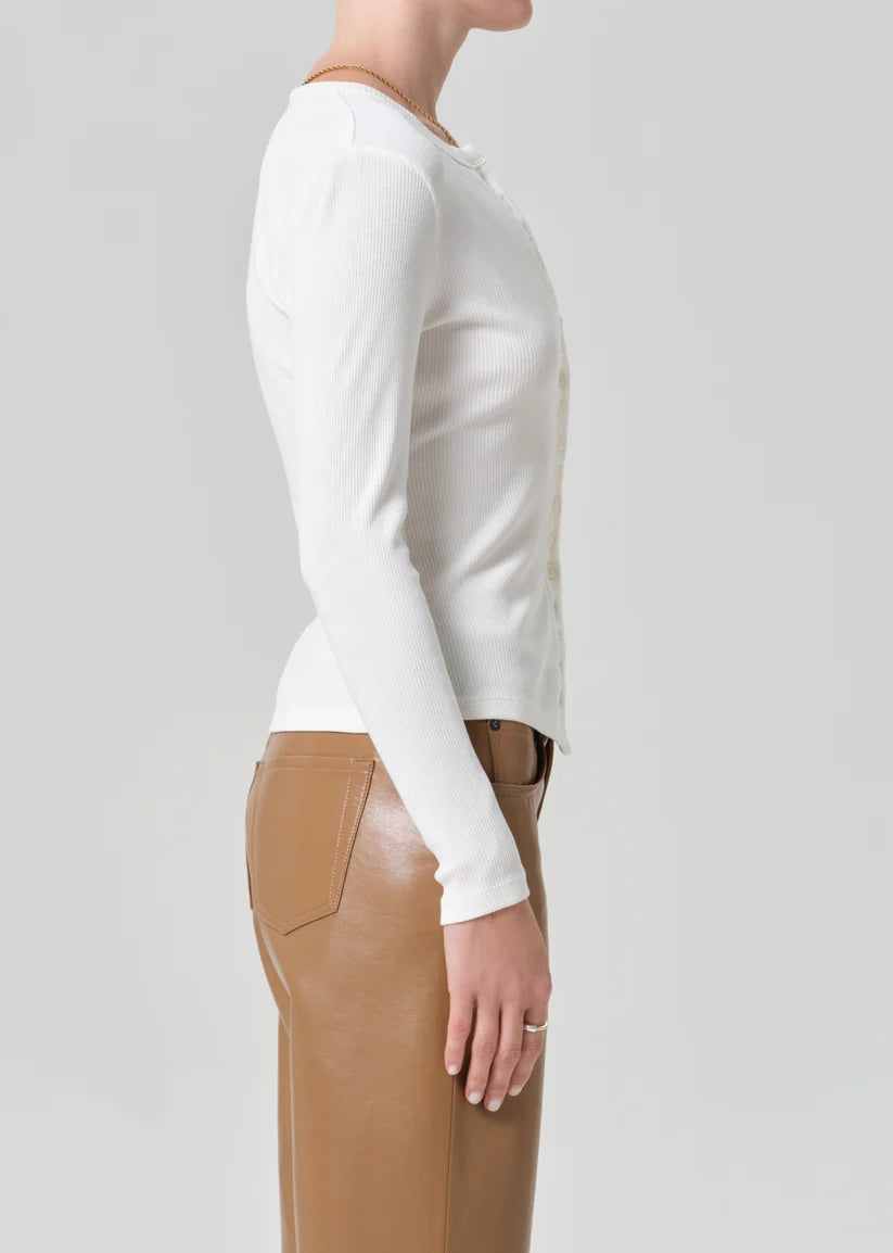 Person wearing a white long-sleeve top and brown pants on a light gray background
