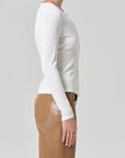 Person wearing a white long-sleeve top and brown pants on a light gray background