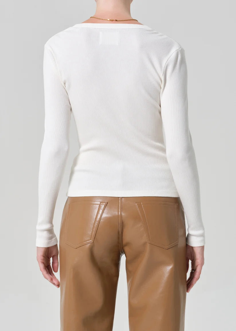 Person wearing a white long-sleeve top and brown pants on a gray background