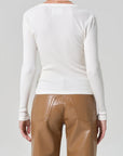 Person wearing a white long-sleeve top and brown pants on a gray background