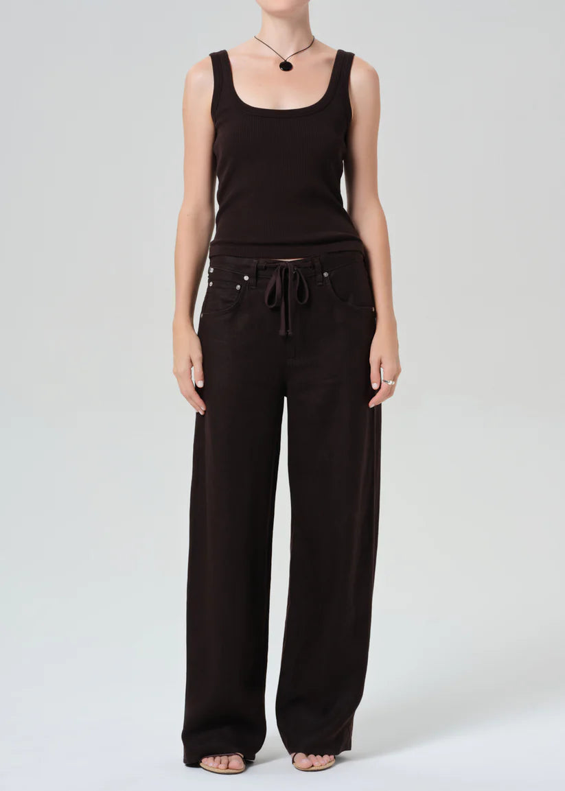 Person wearing a brown sleeveless top and wide-leg pants on a white background
