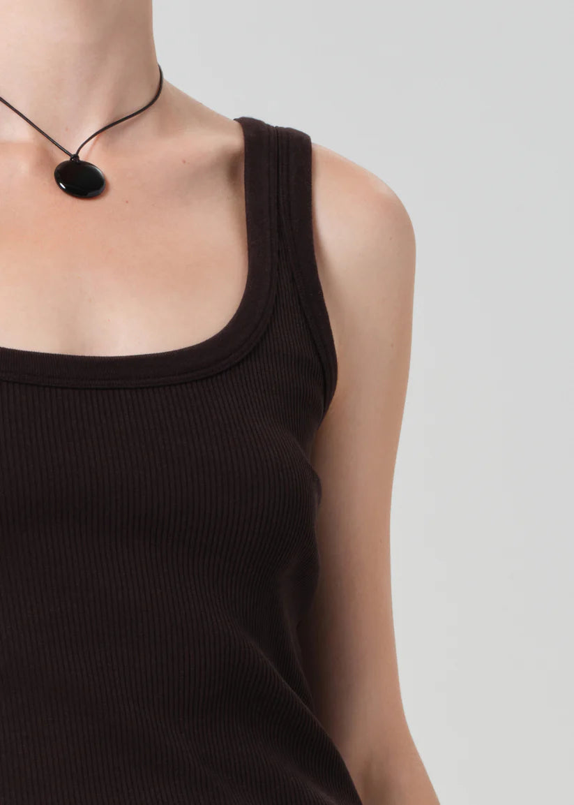 Person wearing a brown tank top and necklace on a plain background