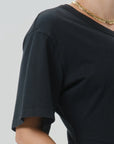 Close-up of a person wearing a black short-sleeve crew-neck T-shirt and a chunky gold chain necklace against a light gray background.