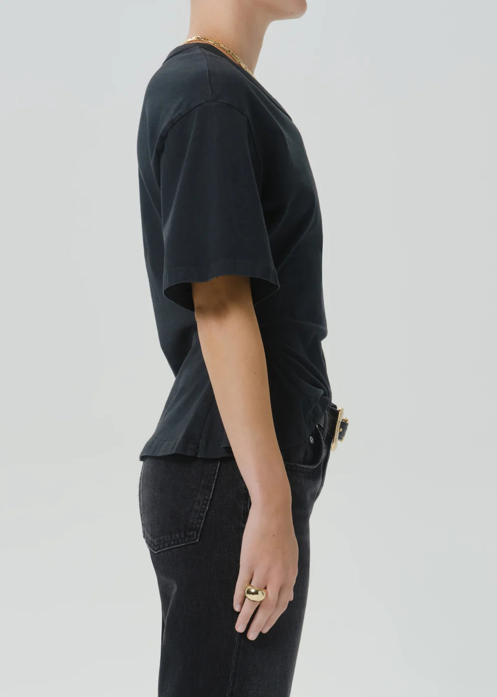 Side profile of a person wearing a black short-sleeve t-shirt and black jeans against a light gray studio background.