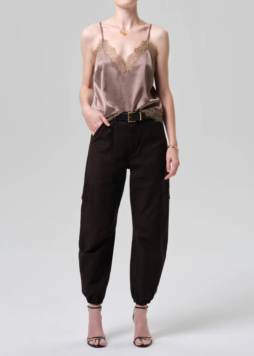 Woman wearing a beige lace camisole and black cargo pants on a white background