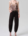 Woman wearing a beige lace camisole and black cargo pants on a white background