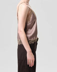 Person wearing a brown lace-trimmed top and dark pants on a light gray background