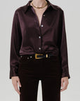 A model wearing a dark brown satin button-down shirt tucked into dark brown corduroy trousers with a gold belt, against a light gray studio background.