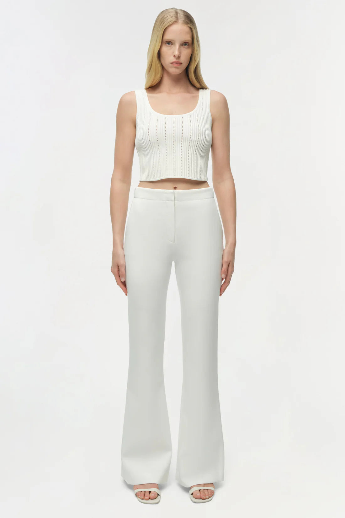 Woman wearing a white sleeveless top and pants on a white background