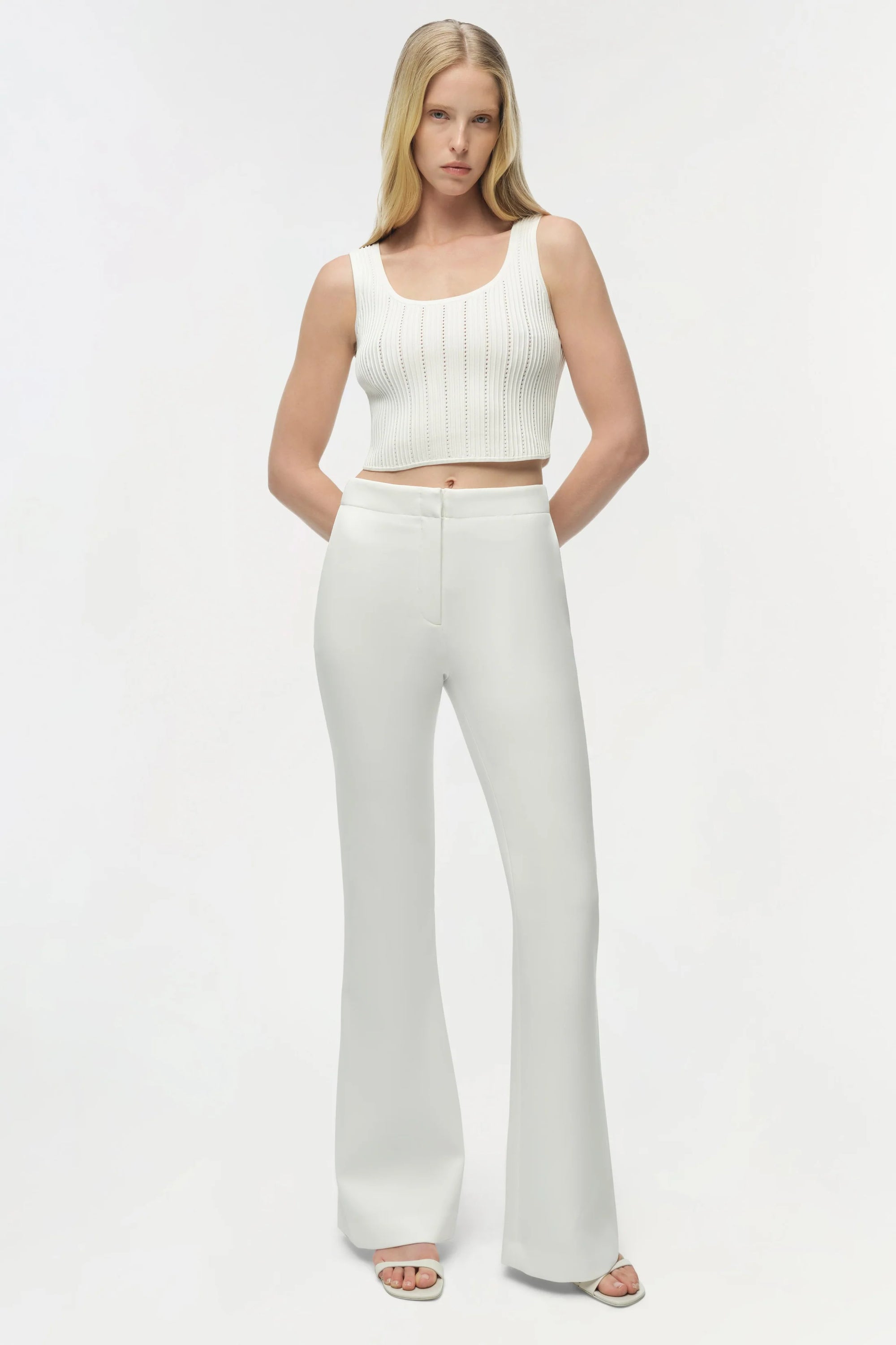 Woman wearing a white sleeveless top and high-waisted pants on a white background