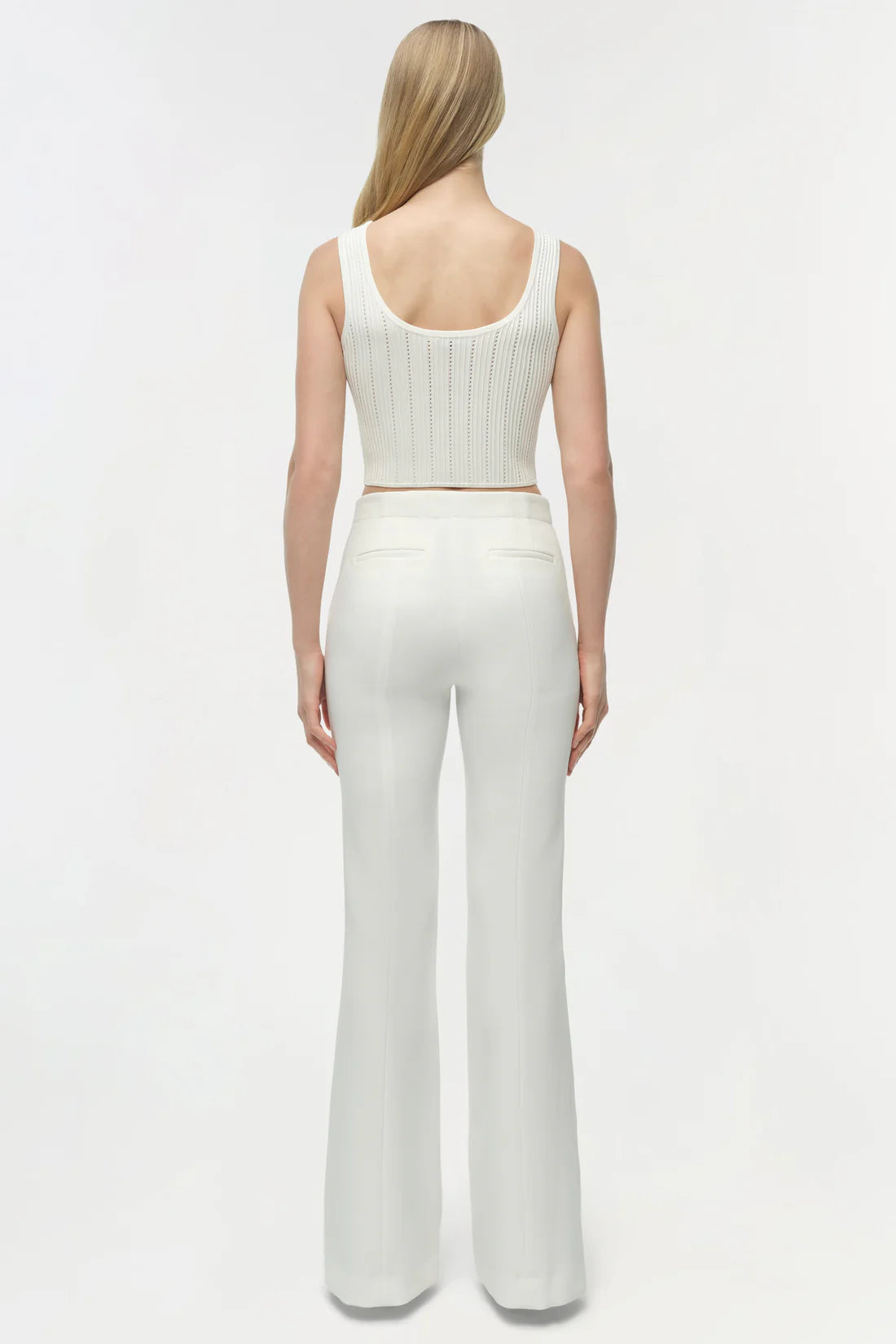 Woman wearing a white ribbed tank top and wide-leg pants on a light gray background