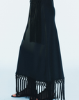 model wearing a black maxi skirt with fringe trim on a white background, side view