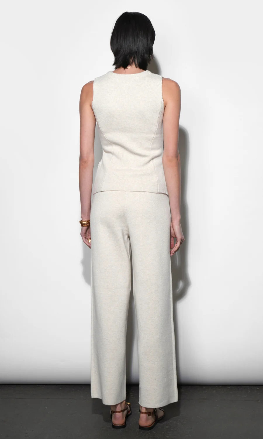 Person wearing a white sleeveless top and wide-leg pants against a plain background