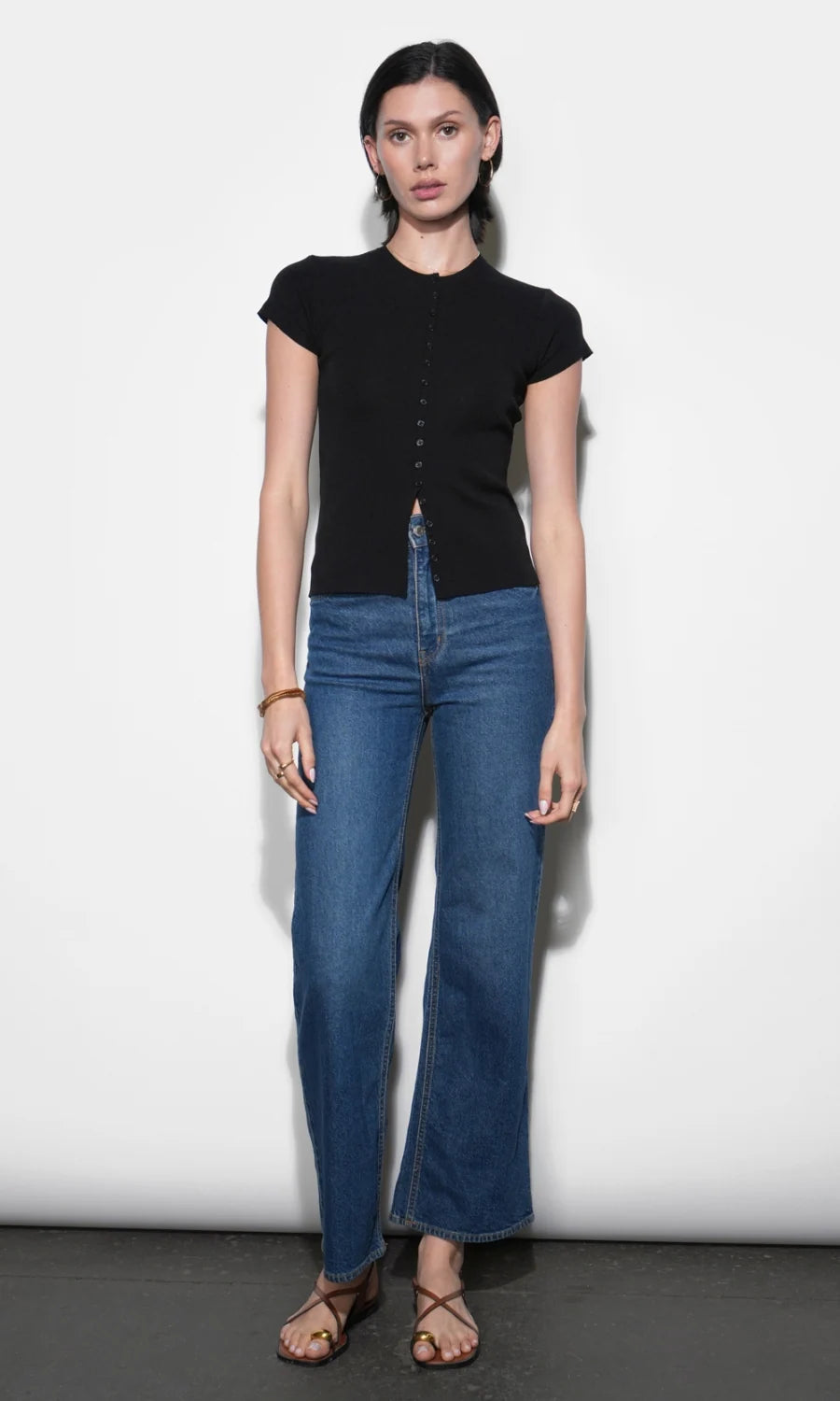Woman wearing a black top and blue jeans against a white background