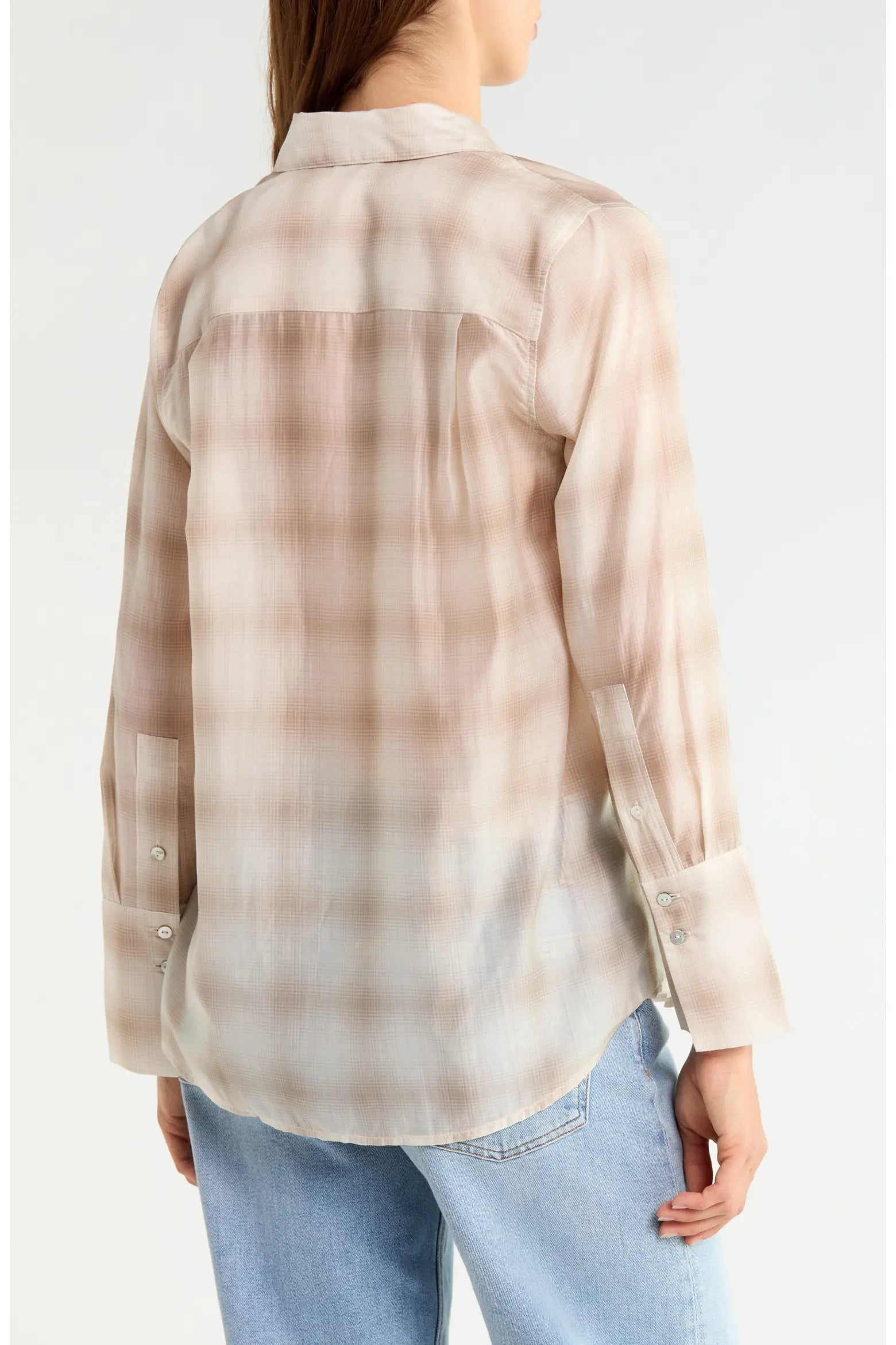 A woman shown from the back wearing a semi-sheer long-sleeve button-up shirt with a beige and light brown plaid pattern, paired with light blue jeans, against a plain white background.