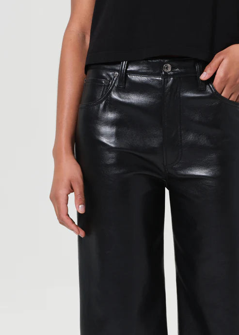 Person wearing black leather pants on a plain background