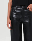 Person wearing black leather pants on a plain background