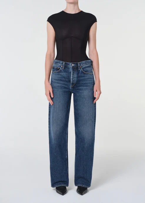 Person wearing a black sleeveless top and blue jeans on a white background