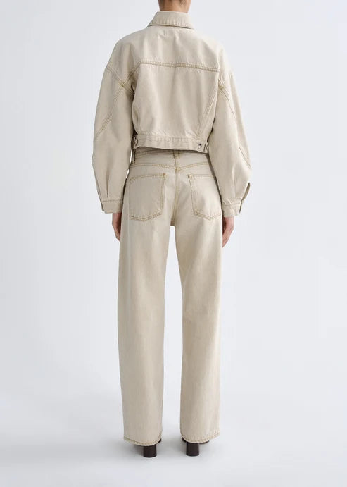A model shown from the back wearing a light beige cropped denim jacket and matching wide-leg denim jeans against a plain light gray studio background.