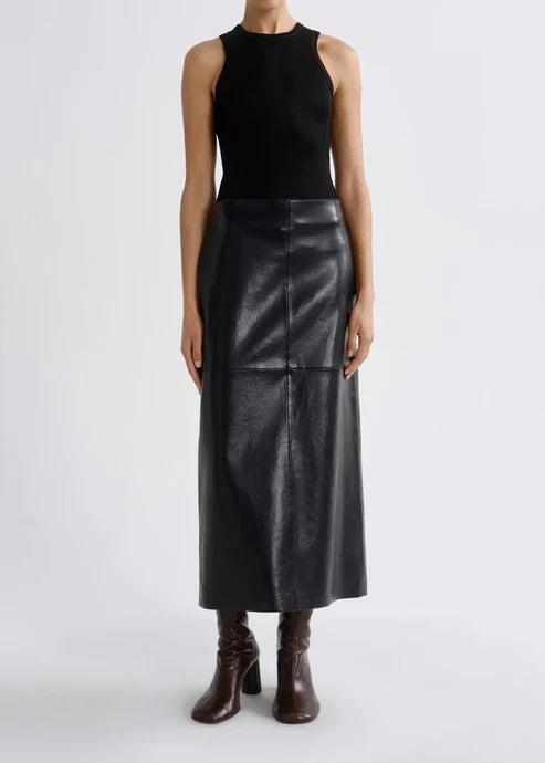 A model wearing a black sleeveless knit top and a black faux-leather midi skirt, paired with dark brown heeled ankle boots, against a light gray studio background.