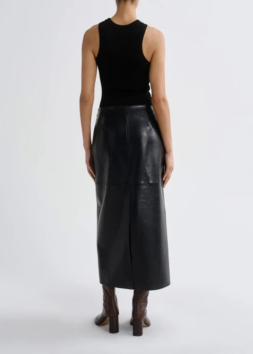A model shown from the back wearing a black sleeveless ribbed top and a black leather midi skirt, paired with brown heeled boots, against a light gray studio background.