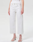 White cropped wide-leg jeans worn by a model, paired with a white top and white heeled thong sandals, photographed against a light gray studio background.