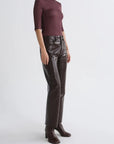 A model wearing a fitted burgundy three-quarter sleeve top, dark brown faux-leather straight-leg pants, and dark brown heeled ankle boots, photographed against a light gray studio background.