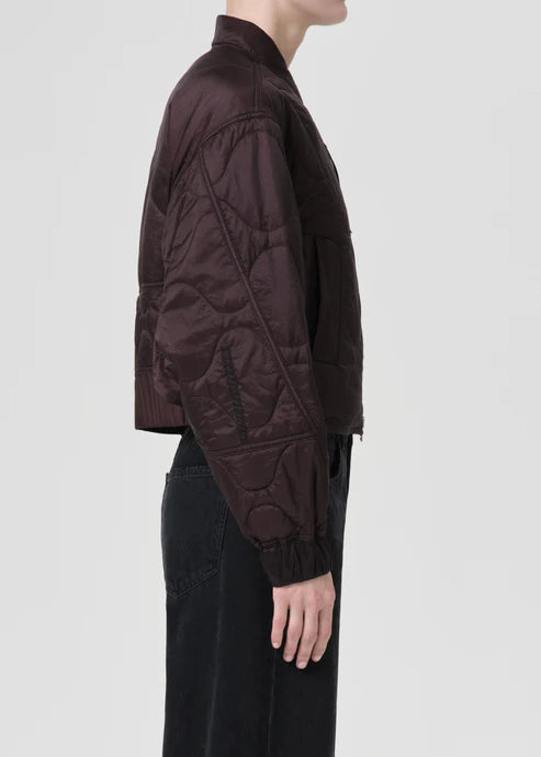 Person wearing a dark quilted jacket on a light gray background, side