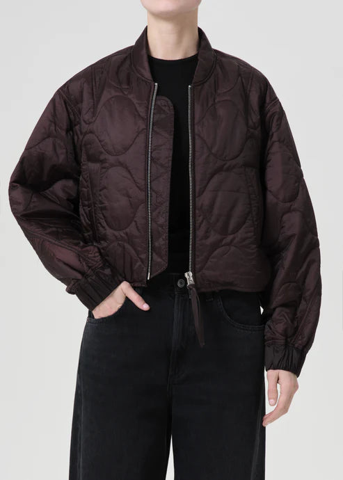 Person wearing a dark brown quilted jacket on a light gray background