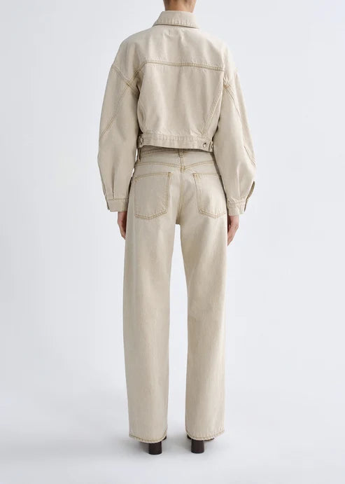 A model shown from the back wearing a light beige cropped denim jacket and matching wide-leg jeans against a plain light gray studio background.