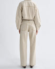 A model shown from the back wearing a light beige cropped denim jacket and matching wide-leg jeans against a plain light gray studio background.