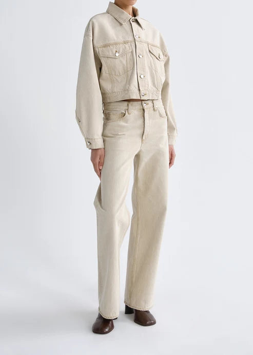 A model wearing a light beige cropped denim jacket and matching straight-leg jeans, paired with dark brown leather shoes, against a plain white studio background.