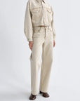 A model wearing a light beige cropped denim jacket and matching straight-leg jeans, paired with dark brown leather shoes, against a plain white studio background.