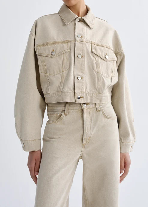 Person wearing a beige denim jacket and jeans on a white background