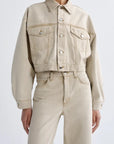 Person wearing a beige denim jacket and jeans on a white background