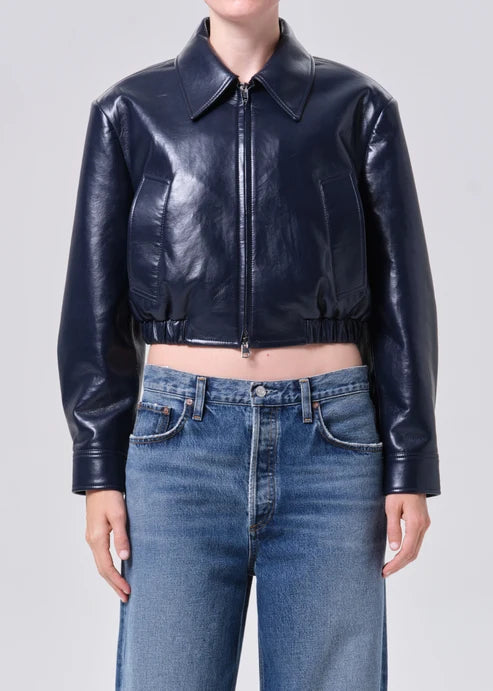Person wearing a black leather jacket and blue jeans on a plain background