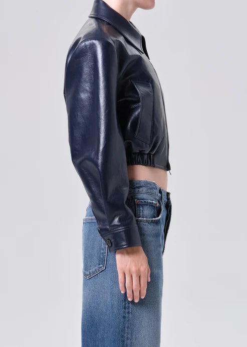 Person wearing a black shiny jacket and blue jeans on a light gray background
