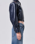 Person wearing a black shiny jacket and blue jeans on a light gray background