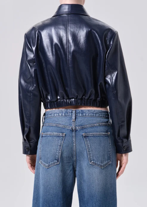 Person wearing a black leather jacket and blue jeans on a plain background