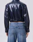 Person wearing a black leather jacket and blue jeans on a plain background