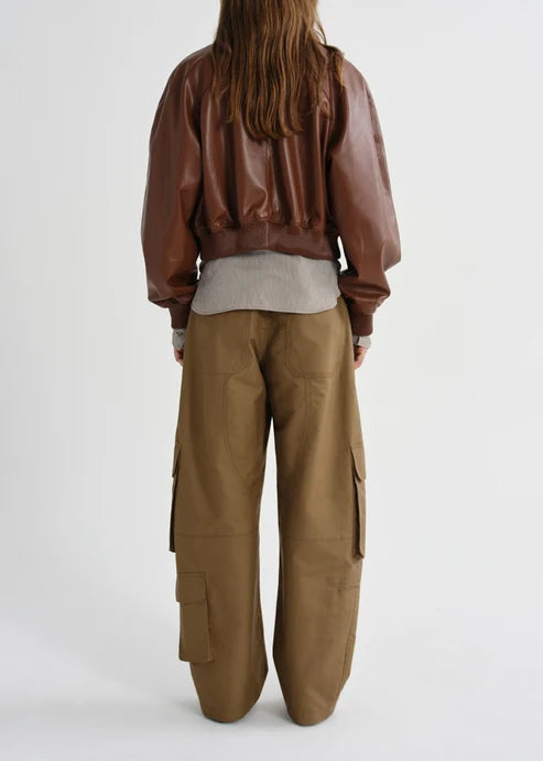 A model shown from the back wearing a brown faux-leather bomber jacket, a light gray t-shirt, and wide-leg brown cargo pants against a plain white studio background.