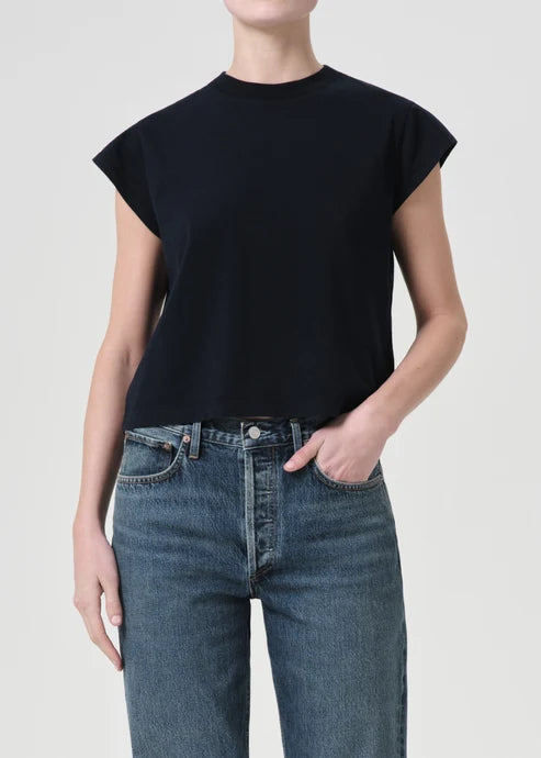Person wearing a black sleeveless top and blue jeans on a plain background