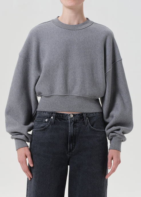 Person wearing a gray cropped sweatshirt and dark jeans on a plain background