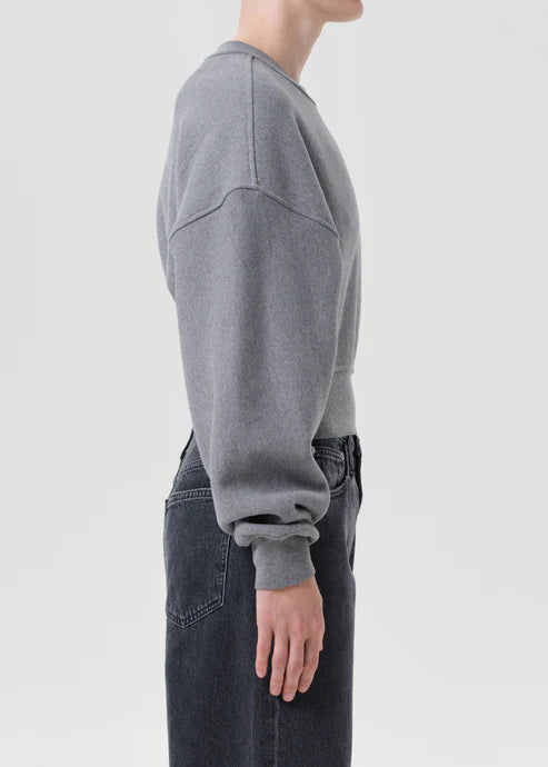 Person wearing a gray sweatshirt and dark jeans on a light gray background, side