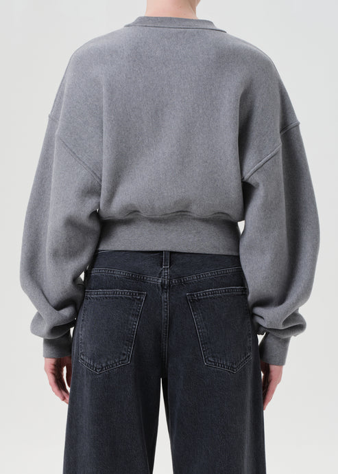 Person wearing a gray sweatshirt and dark jeans on a plain background, back