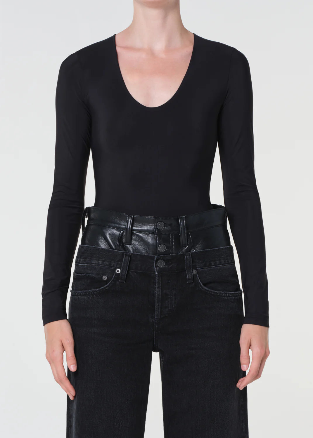 Person wearing a black long-sleeve top and black leather pants on a white background