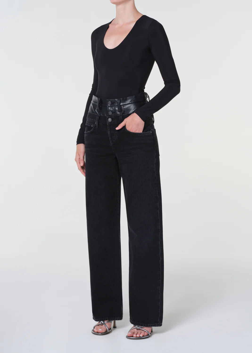 Person wearing a black long-sleeve top and black high-waisted jeans on a white background