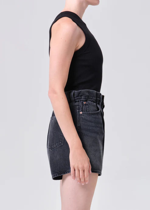 Person wearing a black sleeveless top and black denim shorts on a white background